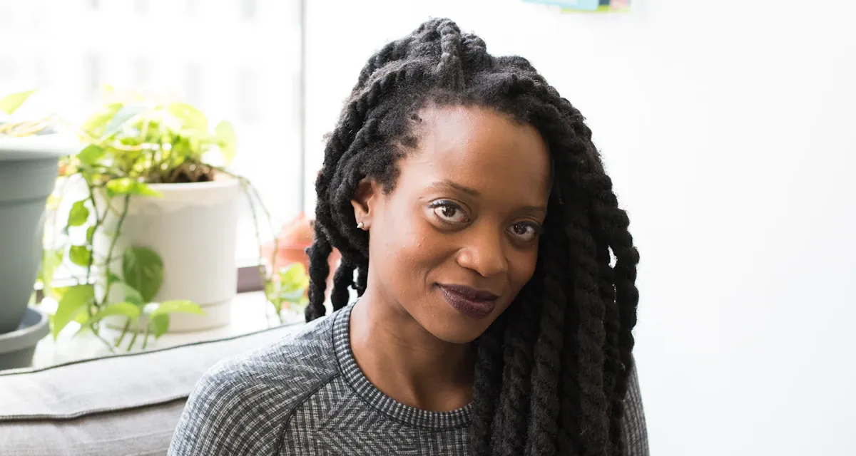 A woman with long braids sitting on a sofa with a laptop