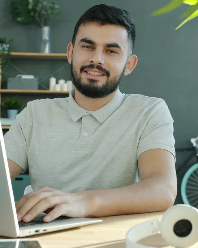 A bearded man smiling at the camera while working on a laptop