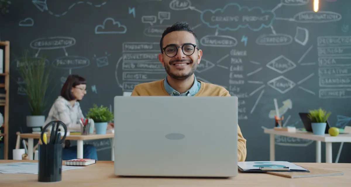 A smiling man at a desk with a laptop in a bright office